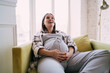 © BullRun - Cheerful pregnant woman resting on sofa in living room