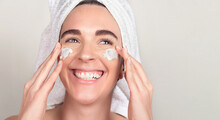Happy Woman With Towel Wrapped Head Applying Cosmetic Mask And Cream