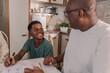 © Brastock Images - Brazilian boy sitting in the kitchen smiling to his father who is helping him with his homework in Brazil