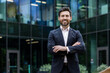 © Tetiana - Portrait of mature adult businessman, senior boss with beard smiling and looking at camera, experienced and successful man in business suit outside office building with crossed arms