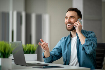 Aufkleber - Cheerful Young Man Talking On Cellphone, Sitting At Workplace In Modern Office