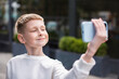 © cenchild - focus on face of smiling boy taking selfie self portrait photos on smartphone, posing on street