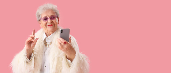 Sticker - Stylish senior woman in fur coat using mobile phone on pink background with space for text