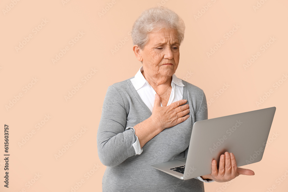 Upset senior woman with laptop on beige background