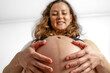 © Michael - Low angle close up of smiling pregnant woman with naked round belly at home. Last month of pregnancy - week 36. White background.