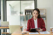 © ArLawKa - Asian businesswoman in suit sitting on desk in office, with computer document graph for bookkeeping in workplace to calculate annual profit by function, business concept