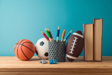 Back to school concept with pencils, basketball ball, football ball and books on wooden table over blue background