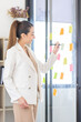 © David - Young Creative business asian woman writing on sticky notes on a glass wall, female colleague looking.