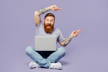 full body young redhead bearded man in violet t-shirt casual clothes sitting hold use work on laptop