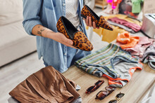Ethical Consumption, Exchange, Cropped View Of Young Tattooed Woman Holding Stylish Animal-print Shoes Near Sunglasses And Garments On Table, Sustainable Living And Mindful Consumerism Concept