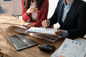 Team of two asian male and female business people working together discussing new financial graph data on office table with laptop and digital tablet.