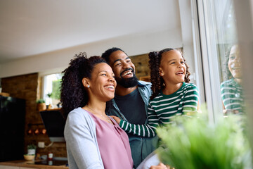 Wall Mural - Cheerful black girl and her parents looking out of window at home.