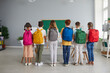 © Studio Romantic - Back to school. Six small schoolchildren stand in row with large colorful fashionable backpacks on their shoulders. Rear view of boys and girls in casual clothes posing in classroom with school bags.