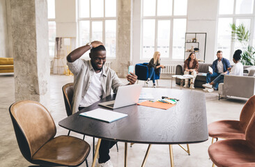 Sticker - Cheerful black man using mobile phone at creative workspace