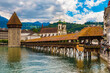 The famous covered timber footbridge Kapellbrücke (Chapel Bridge) with Water Tower over the river Reuss at the street Rathausquai. The Jesuit Church St. Francis Xavier can be seen in the background.