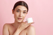 © master1305 - Portrait of young beautiful woman posing with face moisturizing cream against pink studio background. Skin hydration. Concept of natural female beauty, body and skincare, cosmetology, health, ad