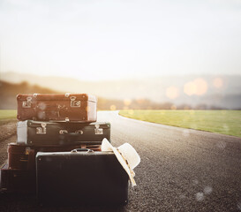 luggage resting on asphalt with background a road at sunset