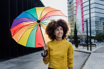 Wall Mural - young African American woman homosexual with rainbow flag or umbrella in city of Latin America, Hispanic and caribbean LGBT female with afro hair