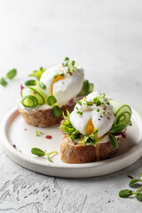 Poached egg sandwich with cucumber and microgreens. Healty breakfast bruschetta on light background. Keto diet, text space