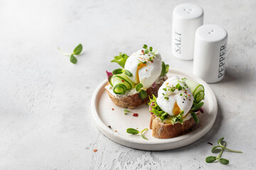 Poached egg sandwich with cucumber and microgreens. Healty breakfast bruschetta on light background. Keto diet, text space