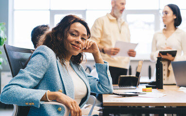 Wall Mural - Portrait of successful female entrepreneur 30s smiling at camera during collaboration day in office interior, happy African American employee dressed in smart casual apparel posing in workspace