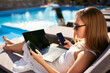 Woman doing remote multitasking work with multiple electronic internet devices on swimming pool beach bed. Freelancer businesswoman telecommuting with tablet, cellphone and laptop from tropical island