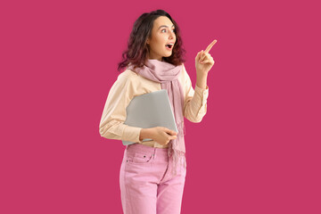 Poster - Surprised young woman in scarf with laptop pointing at something on pink background