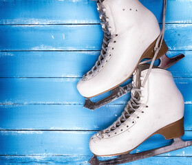 a pair of worn white leather skates for figure skating on a blue wooden background, empty space on the left