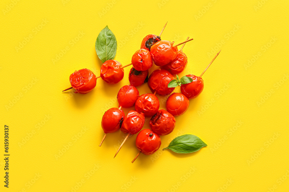 Skewers with tasty grilled tomatoes and basil on yellow background