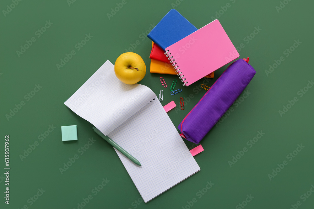 Notebooks with fresh apple and different stationery on green background