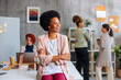 © bernardbodo - Beautiful African-American business woman sitting in office and looking sideway while female colleagues work in background.