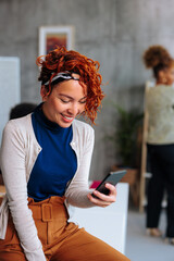 portrait of young hispanic woman smiling while using phone during work in office.