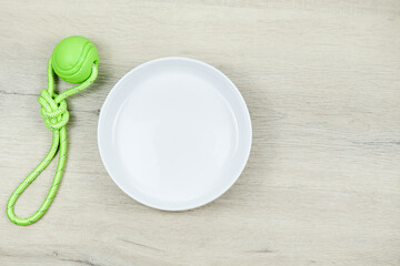 White empty dog food bowl on grey background with green toy ball, top view