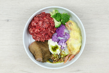 Wall Mural - Natural dog food. Fresh raw meat, chicken, vegetables and food supplements in bowl on grey background. Top view