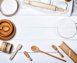 Wall Mural - wooden round plates, sieve and rolling pin, round cutting board and other kitchen items on a white table, top view, empty space in the middle