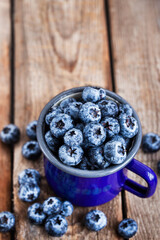 Wall Mural - Fresh ripe blueberries and in blue enamel mug on rustic background