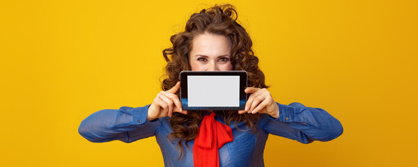 Wall Mural - modern woman with long wavy brunette hair hiding behind tablet PC blank screen on yellow background