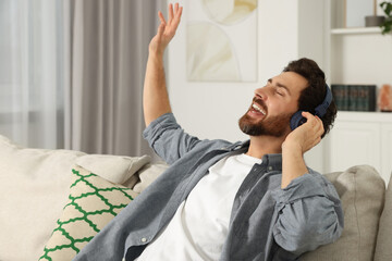 Poster - Happy man listening music with headphones on sofa indoors