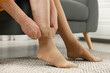 Woman putting on compression stocking in living room, closeup. Prevention of varicose veins