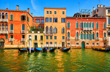 Wall Mural - Venice, Italy. Gondolas with floating at piers by Grand Canal among antique buildings and traditional italian Venetian architecture. Sunny evening sunset with blue sky and clouds.