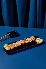 Canvas Print - Gunkan sushi set with crab, shrimp, salmon, tuna, and eel, presented on a black plate against a deep blue curtain background. Ideal for a modern Asian restaurant menu