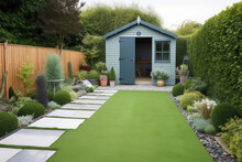 A General View Of A Back Garden With Artificial Grass, Grey Paving Slab Patio, Flower Bed With Plants, Timber Fences, Blue Shed, Summer House Garden Timber Outbuilding