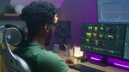 African American colorist edits action movie, makes color correction, works at home. Program interface with RGB tools and wheels on computer and big digital screen. Concept of film post production.