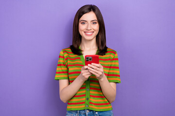 Poster - Portrait of cheerful positive girl with stylish hairdo dressed striped cardigan typing email on smartphone isolated on violet background