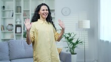 Happy Joyful Young And Attractive Woman Dancing In The Living Room At Home. Active Pretty Curly Brunette Female In A Yellow Shirt Cheerfully Celebrating Achievement. Dance Of A Funny Student
