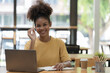 © Songsak C - A young African American stylish woman, freelancer, student, or real estate agent, sitting at her desk at home office, looking at the camera and smiling pleasantly.