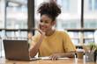 © Songsak C - A young African American stylish woman, freelancer, student, or real estate agent, sitting at her desk at home office, looking at the camera and smiling pleasantly.