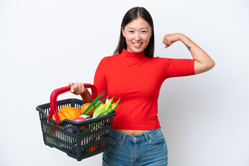 Wall Mural - Young Asian woman holding a shopping basket full of food isolated on white background doing strong gesture