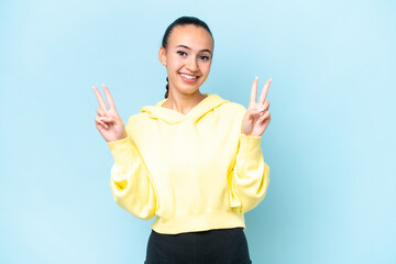 Wall Mural - Young Arab woman isolated on blue background showing victory sign with both hands