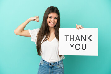 Wall Mural - Young caucasian woman isolated on blue background holding a placard with text THANK YOU and doing strong gesture